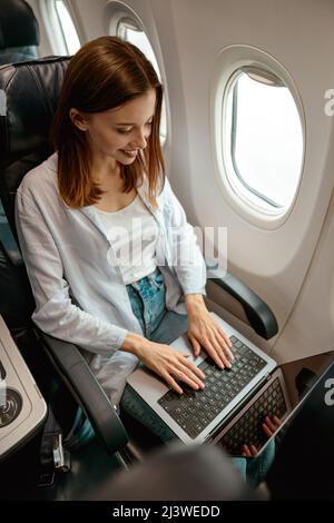 Joyful woman working on laptop in airplane Stock Photo
