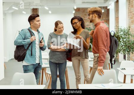 Four students standing and talking in classroom Stock Photo