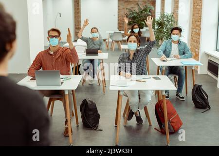 Students in facial protective mask raising hand for answer Stock Photo