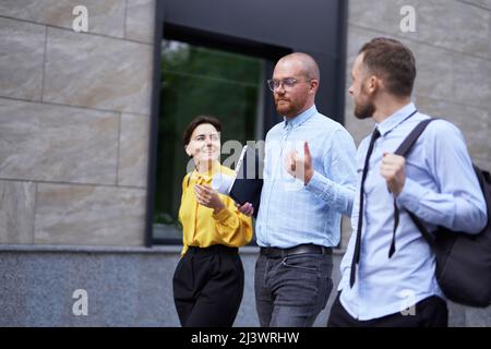 Business people brainstorming or discussing project outdoor walking. Three white collar workers in formal wear walking along the street in downtown near office, urban background. High quality photo Stock Photo