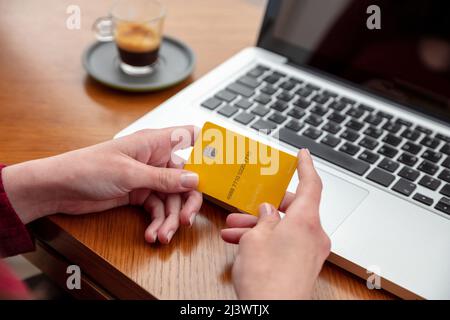 Bank credit card, Female hands holding blank yellow plastic card, online payment and shopping using computer laptop, close up view Stock Photo