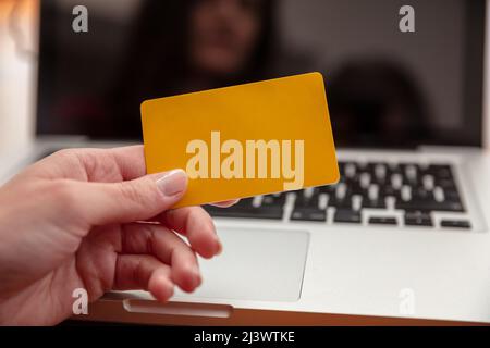 Online shopping, credit card payment. Female hands holding blank yellow plastic card and using computer laptop, close up view, copy space. Stock Photo