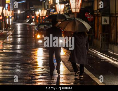Couple carrying umbrellas walks towards taxi on rainy night in historic Kyoto district Stock Photo