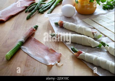 Preparing asparagus wrapped in prosciutto and puff pastry on  wooden table. Spring delicious appetizer. Directly above. Stock Photo