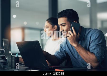 This is my canvas, imma paint it how I want. Shot of a young man using his cellphone while working on a laptop in a modern office. Stock Photo
