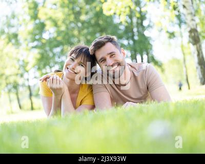 Fun and love concept with mid adult couple lying down in grass looking to camera and smiling Stock Photo
