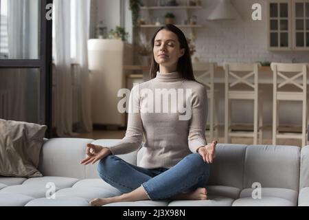 Peaceful yogi girl meditating with closed eyes on home couch Stock Photo