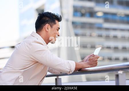 An Asian businessman looks at his digital tablet on office balcony in the city Stock Photo