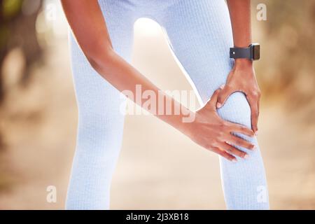 My knee has been acting up. Shot of a woman clutching her knee in pain during a jog. Stock Photo