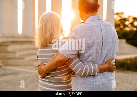 White senior couple hugging and looking at sunset outdoors Stock Photo
