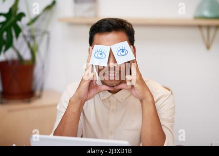 An Asian businessman is stressed at work with eyes drawn on sticky notes  Stock Photo