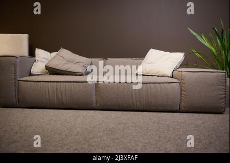 Front view of a large comfortable sofa made of high quality fabrics and soft cushions, on display for sale in the showroom of a furniture store. Home Stock Photo