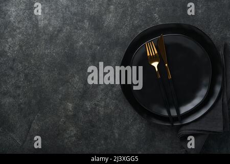 Ceramic empty black plate, silverware and linen kitchen towel napkin on old black ceramic cement concrete table background. Cooking stone backdrop. To Stock Photo