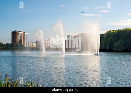 Calm lake in Pildammsparken with three tall fountains with reflection and blue sky in Malmö, Sweden Stock Photo