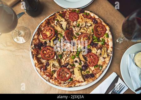 Have a slice. High angle shot of a full plate of pizza resting on top of a table inside of a restaurant during the day. Stock Photo