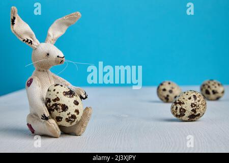 Easter Bunny with spotted quail eggs on a white wooden table on a blue background. Easter festive background Stock Photo