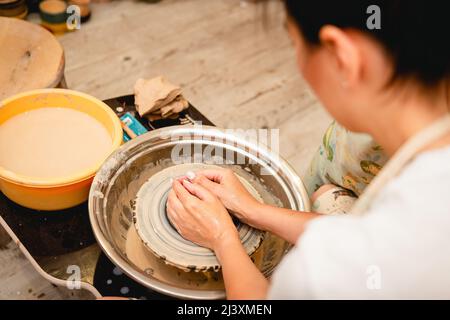 Potter working on potters wheel with clay. Process of making ceramic tableware in pottery workshop. Handicraft and art concept. Stock Photo