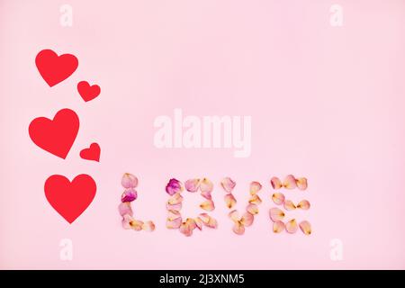 Word love made of pink rose petals and red hearts on pink background. Flat lay, top view. Stock Photo