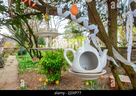 A teapot and cake stand hang from tree branches at a display in a public garden in Penrith, Cumbria, UK resemble the Mad Hatter's tea party Stock Photo