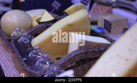 Assorted cheese is on the counter at the fair. ART. Selling homemade cheese lying in baskets at the fair. Cheese collection close-up. Stock Photo