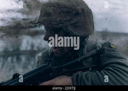Ukrainian soldier stands with kalashnikov assault rifle during artillery bombardment by russian enemy. Concept of russian military invasion in Ukraine Stock Photo