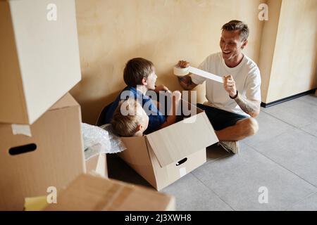 High angle portrait of happy father playing with two sons in cardboard box during family moving house Stock Photo