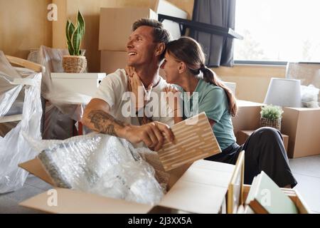 Portrait of happy tattooed couple unpacking boxes sitting on floor while moving into new house, copy space Stock Photo