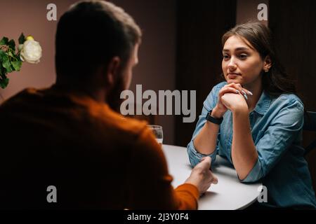Back view unrecognizable loving young man making proposal for marriage to calm pretty woman sitting at table with candles, marry me. Stock Photo