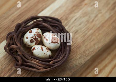 Chocolate nest with three chocolate spotted eggs on a wooden background, copy space Stock Photo