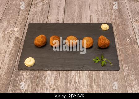Delicious round croquettes of serrano ham on a rectangular black slate plate with mayonnaise and parsley served in a Spanish tapas restaurant Stock Photo