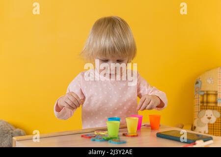 A girl in pink pajamas against a yellow wall enthusiastically