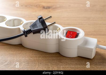 Unplugged electric appliance plug over switched off white power strip on the floor. Power crisis. Increasing the energy and heating costs. Inflation. Stock Photo