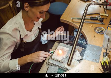 Goldsmith working on a hot glowing ring at her workbench Stock Photo