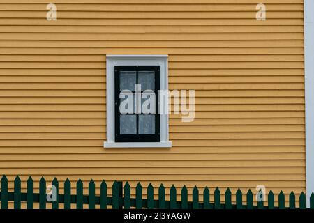 The exterior of a vintage yellow building with a six pane glass window. There's green trim around the window with white lace curtains hanging inside. Stock Photo
