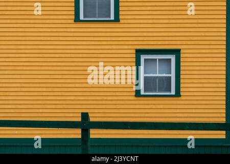 The exterior of a vintage yellow building with a four pane glass window. There's green trim around the window with white lace curtains hanging inside. Stock Photo