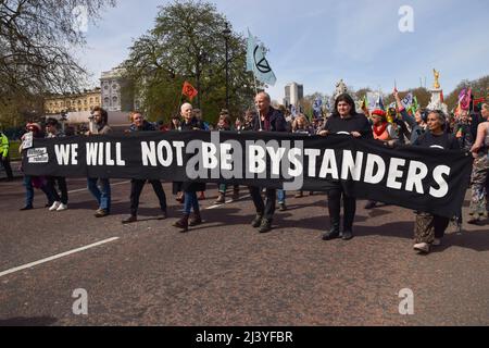 London, UK. 10th April 2022. Protesters march with a 'We will not be bystanders' banner past Buckingham Palace. Extinction Rebellion protesters continue their latest daily campaign, expected to last for more than a week, calling on the government to end fossil fuels and act on climate change. Credit: Vuk Valcic/Alamy Live News Stock Photo