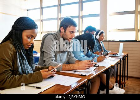 Cellphones are a big distraction. Cropped shot of a group of young university students working in class. Stock Photo