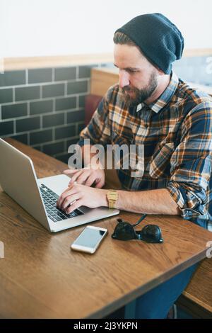 His office away from the office. Shot of a young man using his laptop while sitting in a cafe. Stock Photo