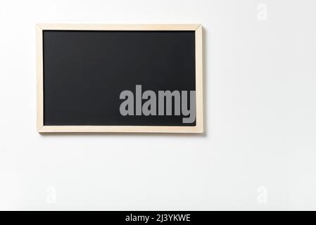 Blank black chalkboard hung on a white wall. Image with copy space, concepts: school, education, training. Stock Photo