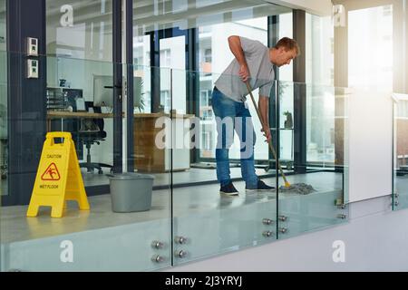 Keeping the office clean. Shot of a young man mopping the office floor. Stock Photo