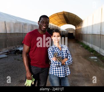Successful confident biracial farmer couple on background of greenhouses Stock Photo