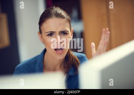 Why is the internet so slow. Shot of a young businesswoman using a computer and looking angry in a modern office. Stock Photo