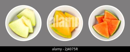 Melon slices, in white bowls, over gray. Galia, honey Cantaloupe melon and watermelon. Freshly cut, triangular shaped pieces. Stock Photo