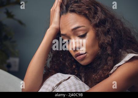 I dont know how Ill get over this. Shot of a young woman looking unhappy while sitting at home. Stock Photo