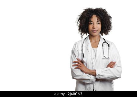 Curly haired African American female doctor wearing uniform standing with arms folded isolated on white background and looking at camera Stock Photo