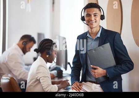 As manager, I always keep my team on track. Portrait of a young call centre agent holding a folder in an office with his colleagues in the background. Stock Photo