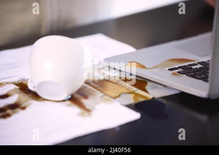 This is going to be quite the mess to fix. Closeup shot of coffee spilt over a laptop and paperwork on a table. Stock Photo