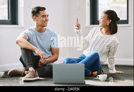 I want to remember this day forever. Full length shot of an attractive young woman sitting and taking photographers of her boyfriend in their new home Stock Photo