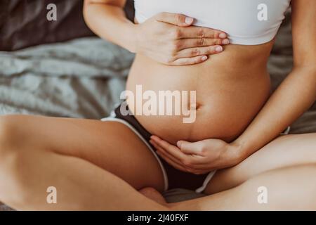 Pregnancy belly stretch marks and linea nigra. Pregnant woman caressing holding stomach during first trimester. Skincare body care health concept Stock Photo