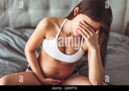 Pregnancy depression. Sad pregnant woman feeling tired or having headache, morning sickness, stress, sleep disorder. Mental health concept Stock Photo